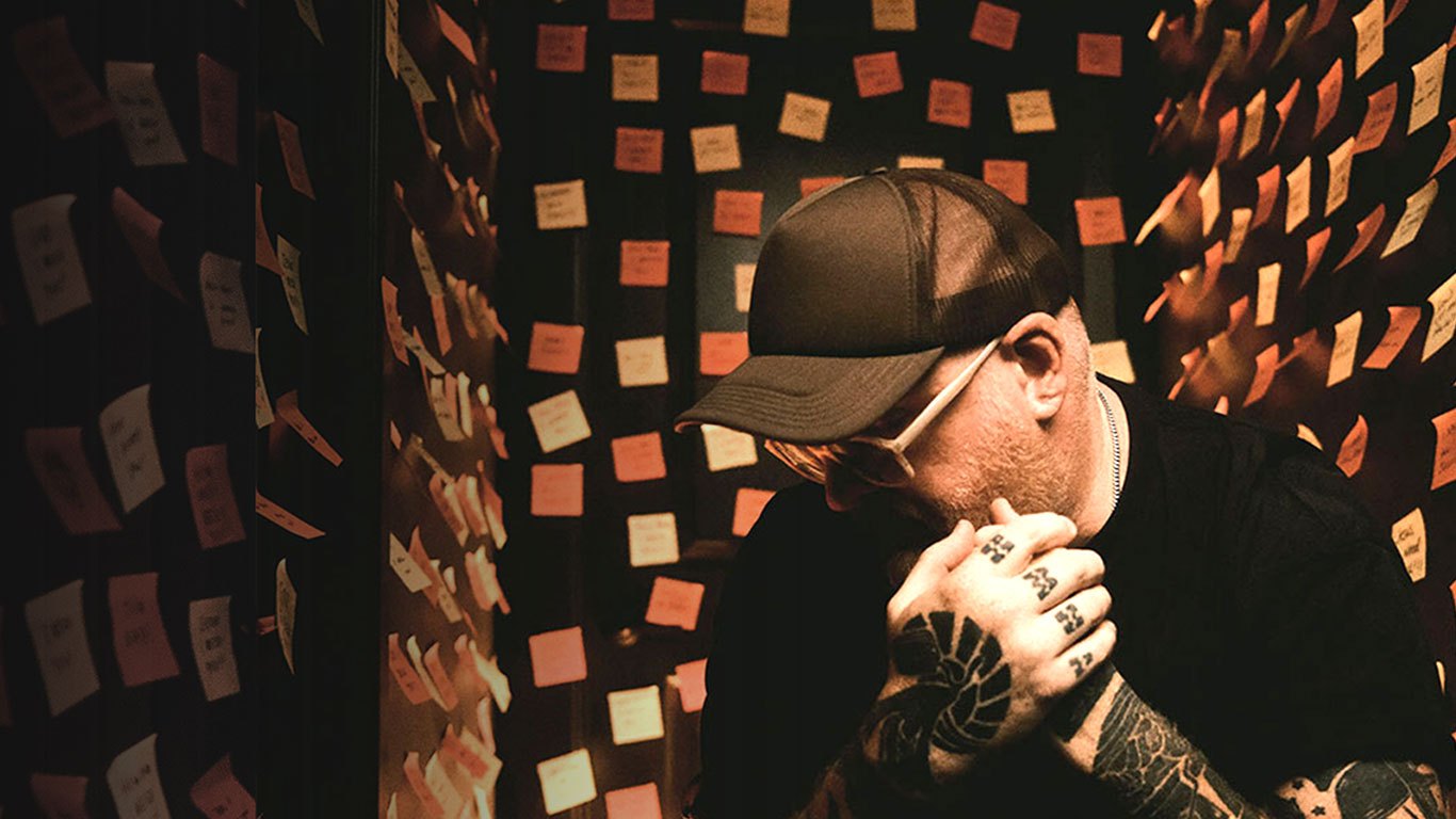 Stephen McWhirter, head bowed and tattooed hands clasped, in a room covered in handwritten sticky notes
